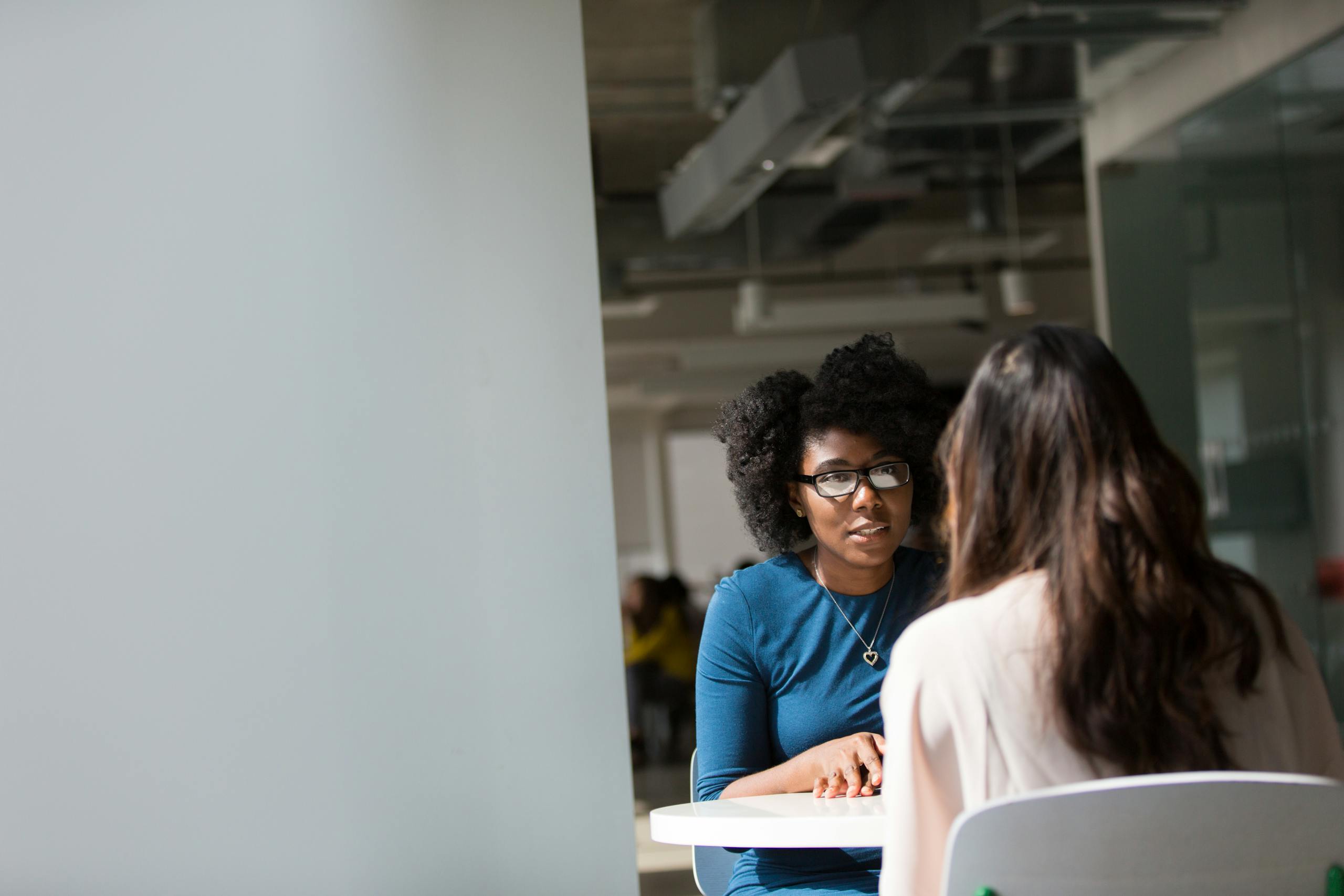 Two women discussing a memorial project at a table in a modern office setting