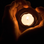 Hands gently holding a lit candle in the dark, symbolising remembrance and digital memorials