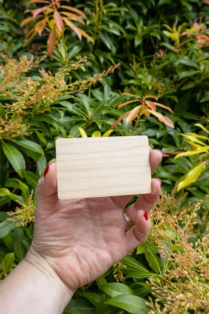 Maple wooden NFC card for a digital memorial, held in hand with green plants in the background to show scale.