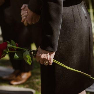 Memorial photography: close-up of hands placing flowers by a candle and framed photo, captured discreetly.