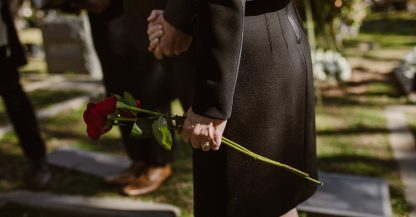 Memorial photography: close-up of hands placing flowers by a candle and framed photo, captured discreetly.