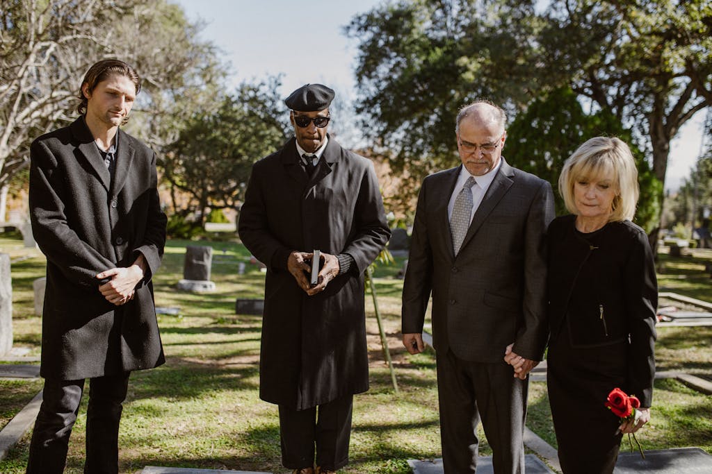 wo men dressed formally at a cemetery during a memorial service, standing among gravestones with trees in the background.